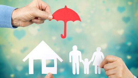 Ein roter Regenschirm aus Papier wird über ein Haus und eine Familie gehalten (Scherenschnitt).