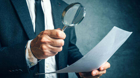 Ein Mann mit Anzug hält eine Lupe vor ein Dokument. Ein Mann mit Anzug hält eine Lupe vor ein Dokument.