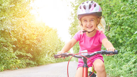 Ein kleines Mädchen mit Helm fährt Fahrrad.