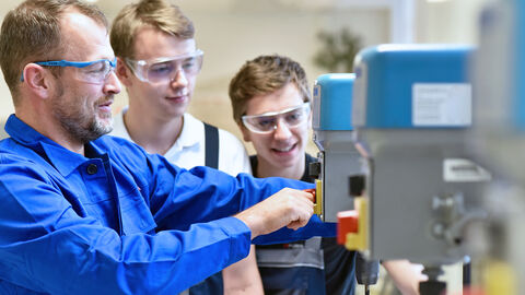 Ein Ausbilder zeigt zwei Auszubildenden einen Arbeitsvorgang in der Produktion.