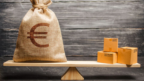 Ein Geldsack und ein paar Kisten stehen auf einer Waage. 