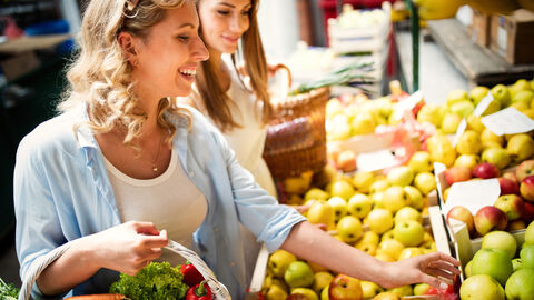 Eine Frau kauft an einem Marktstand Obst und Gemüse.