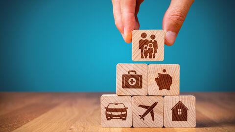 Auf gestapelten Würfeln sind Symbole für Versicherungskonzepte abgebildet.