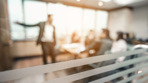 Hinter einer Glasscheibe findet ein Seminar statt.