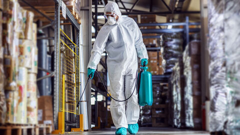 Ein Mann in Schutzanzug und mit Maske desinfiziert ein Lager.