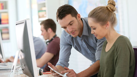 Eine junge Frau arbeitet am Computer während der Ausbilder etwas erklärt.