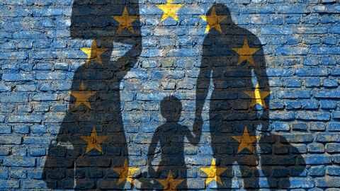 Flüchtlinge werfen ihren Schatten auf eine blaue Mauer mit EU-Sternen.