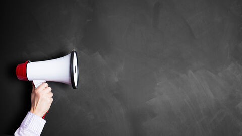 Eine Person hält ein Megafon vor eine dunkle Wand.