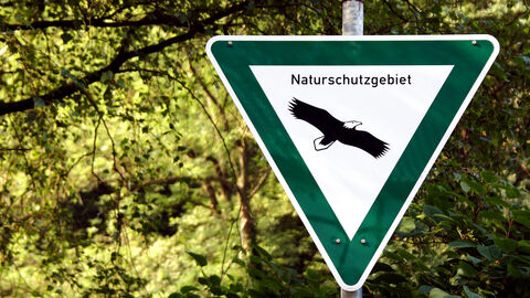 Ein Naturschutzgebiets-Schild steht vor einer Waldfläche.