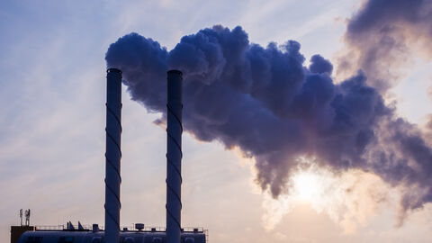 Industrielle Schornsteine rauchen vor blauem Himmel.