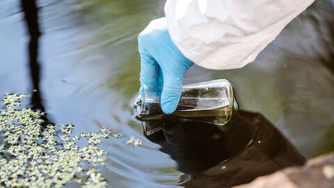 Eine Person im Schutzanzug entnimmt eine Wasserprobe.