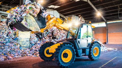 Ein Radlader hebt in einer Recyclinghalle Plastik auf.