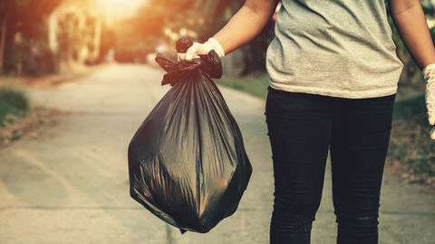 Eine Person mit Handschuhen trägt einen Abfallsack über die Straße.