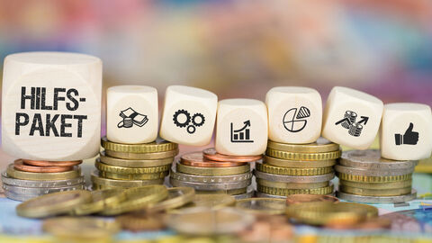 Würfel mit Symbolen zu Hilfspaketen liegen auf Münzen und Geldscheinen. Würfel mit Symbolen zu Hilfspaketen liegen auf Münzen und Geldscheinen.