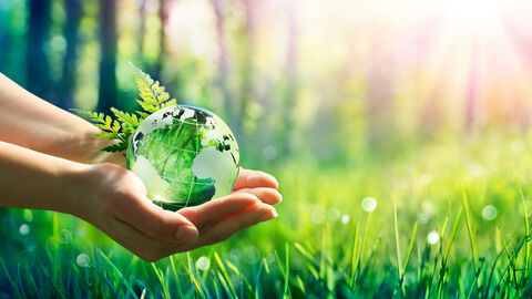 Eine Person hält einen Globus aus Glas über eine Wiese. Eine Person hält einen Globus aus Glas über eine Wiese.