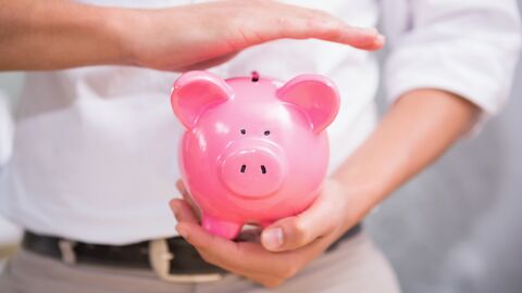 Ein Mann hält die Hand schützend über ein Sparschwein.