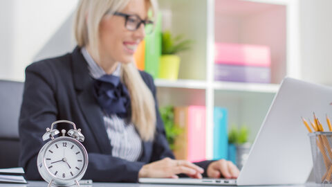 Arbeitszeitgestaltung  Frau arbeitet an Laptop, im Vordergrund steht ein Wecker