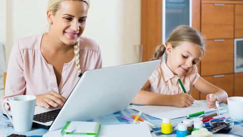 Kinderbetreuung in Betreuungsnotfällen Frau arbeitet im Homeoffice während ein Kind am Tisch malt