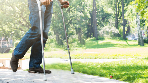Ein Mann läuft mit Krücken durch einen Park.