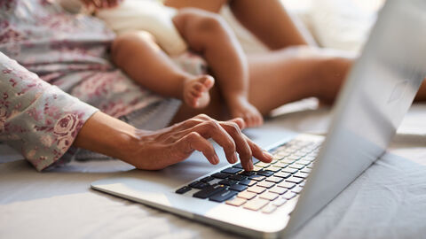 Eine Frau mit Baby im Arm arbeitet am Notebook.