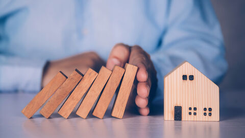 Ein Mann hält fallende Dominosteine mit der Hand auf.