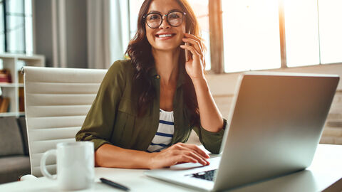 Frau sitzt am Laptop und telefoniert