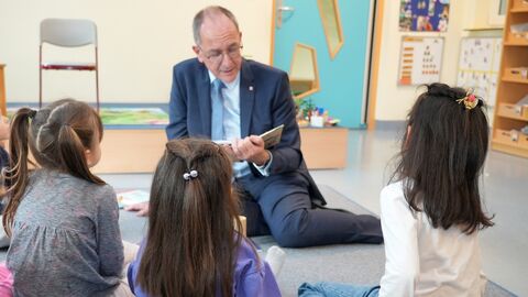 RP Ullrich sitzt in einer Kita auf dem Teppich und liest Kindern aus einem Buch vor
