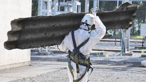 Mann in Schutzausrüstung trägt Asbestplatte weg Mann in Schutzausrüstung trägt Asbestplatte weg