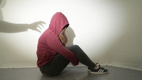 Symbolfoto Eine Frau sitzt auf dem Boden und wird von einer Schattenhand attackiert