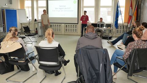 Ein Referent spricht vor mehreren Menschen, die auf Stühlen sitzen