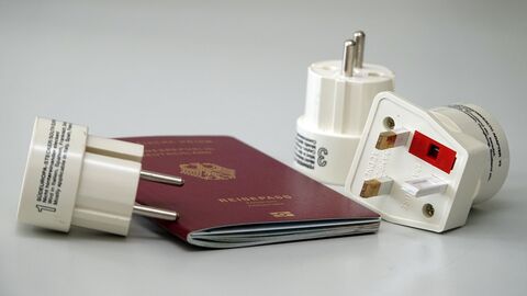 Ein Reisepass und drei Reisesteckadapter liegen auf einem Tisch
