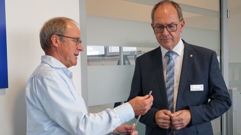 Andreas Schlein (links, Intuitive Surgical Optics) erläutert Regierungspräsident Dr. Christoph Ullrich (rechts) die Anbringung einer Linse auf einem Instrument des da Vinci-Operationssystems.