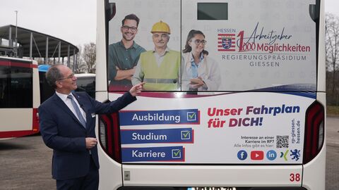 Regierungspräsident Dr. Christoph Ullrich zeigt auf einen Bus, auf dem Werbung für das RP angebracht ist