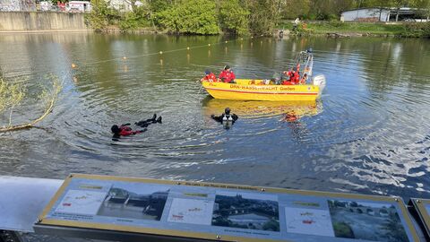 Zwei Taucher in der Lahn und daneben ein Boot der Wasserwacht 