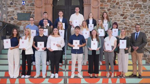 Der kommissarische Regierungsvizepräsident Jan Schneider steht mit den neuen Inspektoranwärtern auf einer Treppe. Zum Erinnerungsfoto halten die Neuen ihre Urkunden in der Hand. 
