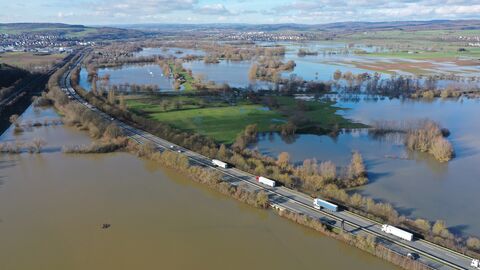 Luftaufnahme einer befahrenen Straße, die von Hochwasser umgeben ist.