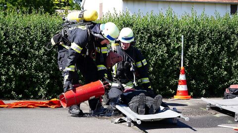 Zwei Feuerwehrleute schütten einer Übungspuppe Wasser aus einer Kübelspritze über.