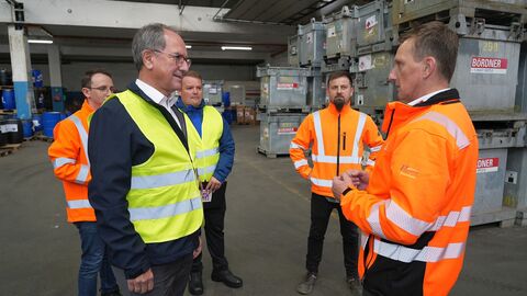 Unternehmensbesuch Fünf Männer stehen in einem Sondermüll-Zwischenlager, in dem alte Spraydosen und Kanister mit Flüssigkeiten stehen.