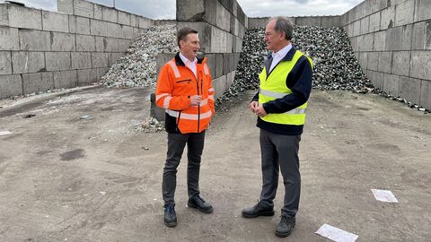 Unternehmensbesuch Zwei Männer stehen vor großen Haufen mit Glasmüll, die von Betonwänden getrennt werden.
