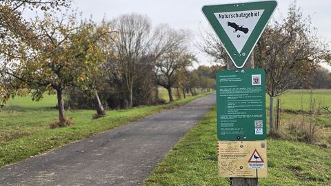 Ein Feldweg, an dem Bäume und ein Schild stehen, das ein Naturschutzgebiet ausweist. 