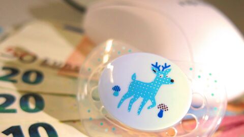 Ein Schnuller liegt auf Geldscheinen und neben einer Computermaus. 