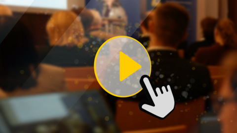 Ein Play-Button mit Mauszeiger. Im Hintergrund sind Menschen von hinten zu sehen, die auf Stühlen sitzen