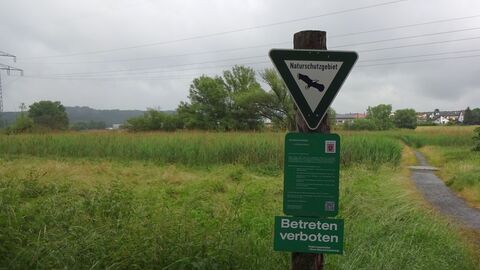 Ein Schild, das auf sas Naturschutzgebiet „Lückebachaue“ bei Pohlheim im Landkreis Gießen hinweist, steht auf einer Wiese.